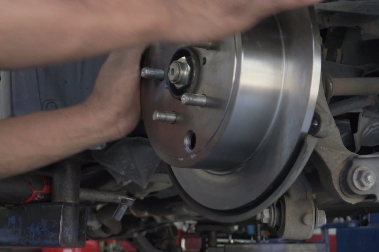 Bay Motors technician fitting a brake rotor onto the hub of a lifted vehicle in Hayward